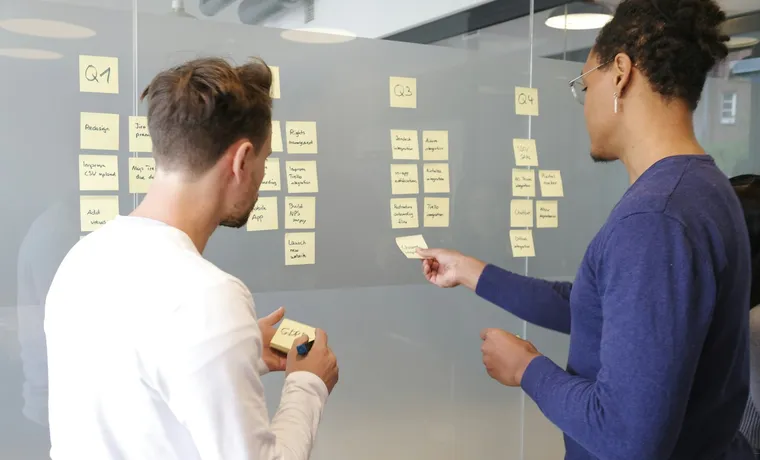 Two people arranging sticky notes on a glass wall