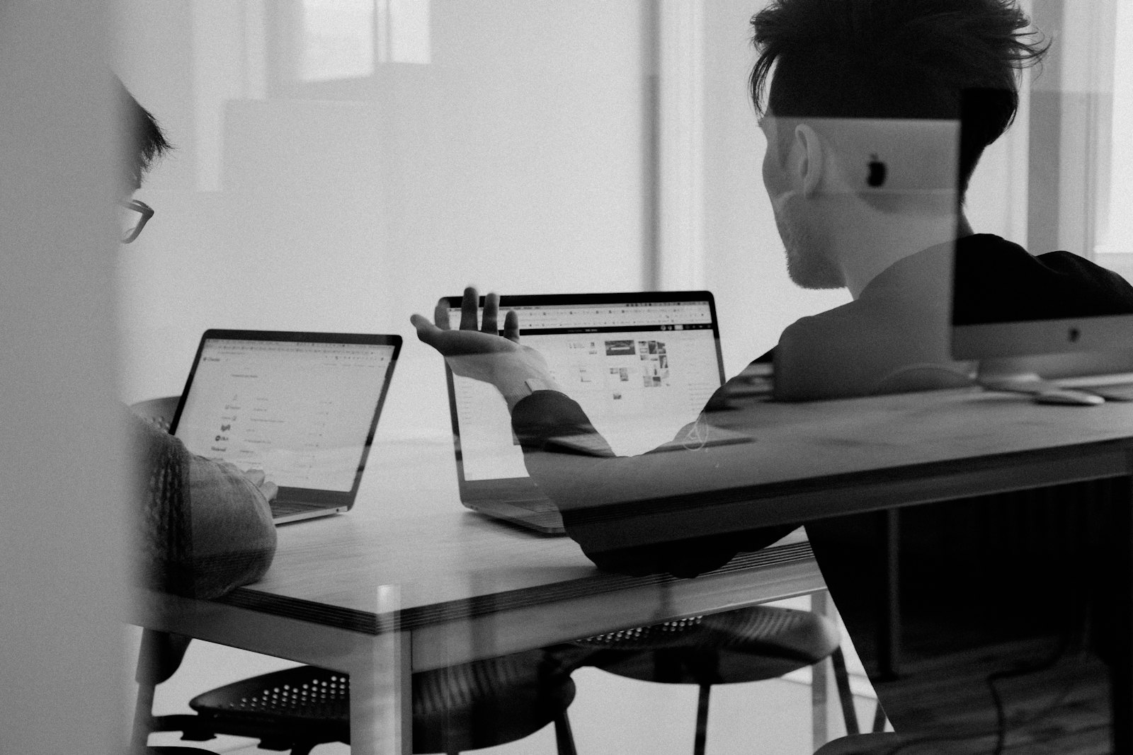 Two people discussing work at a table with laptops